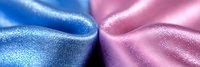 Contrasting blue and pink silky fabric textures meeting in center, creating smooth metallic sheen effect with soft folds and gentle curves. Macro photography for fashion design.