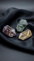 Three raw gemstone crystals including amethyst, fluorite and rutilated quartz arranged on dark fabric for healing meditation and spiritual wellness practices.
