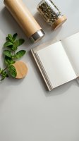 Eco-friendly bamboo thermos bottle with loose leaf tea, fresh mint leaves and blank notebook on neutral background for sustainable lifestyle branding.