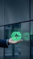 Businessman holding glowing green leaf eco symbol in palm against modern glass building facade, representing sustainability, renewable energy, and environmental responsibility in corporate business.