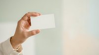 Hand holding blank white business card against neutral background for branding mockup and corporate identity presentation purposes.