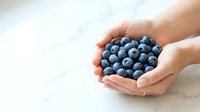 Hands holding fresh blueberries on white marble surface. Organic fruit harvest, healthy eating, and natural food concept for culinary and wellness projects.
