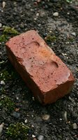 Old weathered red brick lying on mossy asphalt ground with natural texture and rustic patina for construction and building material concepts.