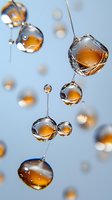 Amber liquid droplets suspended in air against light blue background, creating translucent spheres with reflective surfaces and delicate connecting strands.