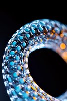 Macro photography of glass art with blue bubble pattern and orange light reflections against dark background, creating ethereal abstract design effect.