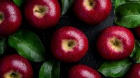 Fresh ripe red apples with water drops and green leaves arranged on dark background, top view. Natural organic produce for healthy eating and cooking.