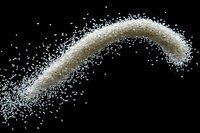 White sugar granules scattered in arc shape against black background, creating dynamic motion effect for food and beverage industry designs.