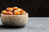 Fresh dates in rustic stone bowl on dark background with copy space, healthy natural dried fruit snack for vegetarian nutrition and energy boost.