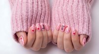 Pink knitted sweater sleeves with hands showing Valentine's Day nail art featuring hearts and romantic designs for seasonal beauty content.