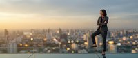 Confident businesswoman in suit standing on rooftop overlooking city skyline at sunset, urban professional lifestyle and career success concept.