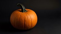 Fresh orange pumpkin with green stem on dark background for autumn harvest decoration, Halloween design, and seasonal cooking projects.