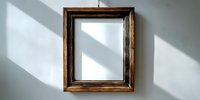 Empty vintage wooden picture frame hanging on white wall with natural sunlight casting diagonal shadows, creating minimalist home decor atmosphere.