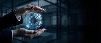 Businessman hands protecting glowing digital security shield icon in modern office environment representing cybersecurity and data protection solutions.