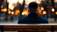 Businessman sitting alone on bench at sunset with city lights bokeh background, contemplating future decisions and career opportunities in urban environment.