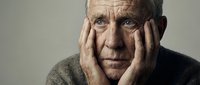 Elderly Caucasian man with hands on face showing depression, loneliness and mental health struggles in dramatic portrait against neutral background.