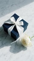 Elegant navy blue gift box with white satin ribbon bow and cream rose on marble surface for special occasions and celebrations.