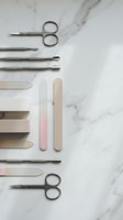 Professional manicure tools set with scissors, files and cuticle pushers arranged on white marble surface for nail care and beauty salon services.