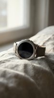 Modern silver smartwatch with leather strap resting on soft bedding near window with natural lighting for technology and lifestyle concepts.