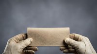 Hands in work gloves holding blank cardboard box against gray background, suitable for packaging, shipping, delivery, and logistics concepts.