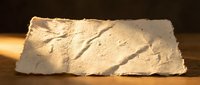 Ancient stone tablet with carved hieroglyphic inscriptions and weathered surface texture on wooden background for historical research projects.