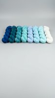 Colorful yarn skeins arranged in gradient from deep blue to white on neutral background for crafting and knitting projects.