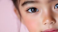 Close up portrait of young Asian female face with natural makeup and clear skin against pink background, showing bright eyes and soft expression.