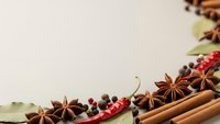 Aromatic spices and herbs arranged on neutral background with cinnamon sticks, star anise, peppercorns and bay leaves for culinary cooking designs.