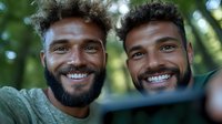Two cheerful African American men with beards and curly hair taking selfie outdoors in natural setting, showing genuine smiles and friendship. Green foliage background.