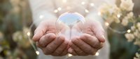 Cupped hands holding glowing crystal sphere with magical light effects and bokeh background for spiritual healing and energy concepts.