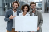 Diverse business team of young professionals holding blank white board for your message in modern corporate environment.