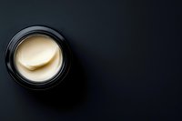 Open black jar of luxury face cream on dark background, top view with copy space for skincare and beauty product promotion.