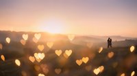 Romantic sunset landscape with heart-shaped bokeh lights and silhouette couple in distance creating dreamy Valentine's atmosphere for love concepts.