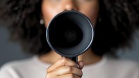 Young African American woman with curly hair holding megaphone in front of face, speaking out concept for activism, leadership and voice amplification.