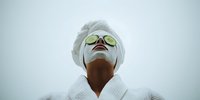 Young woman with cucumber slices on eyes wearing white bathrobe and towel enjoying spa treatment for skincare and relaxation wellness routine.