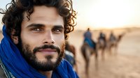 Young bearded man with blue scarf in desert landscape, camels in background during golden sunset. Traditional Bedouin style portrait capturing wanderlust and adventure.