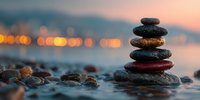 Balanced stone cairn on beach at sunset with blurred city lights in background, symbolizing meditation, wellness, and inner peace.