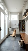 Bright mudroom with slate tile floor, built-in cabinets, pet wash station, golden retriever and fluffy cat, natural light, organized storage.