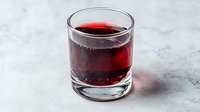 Glass of dark red cranberry juice with bubbles on marble surface for healthy drinking and nutrition concepts.