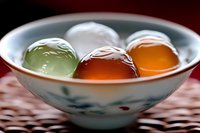 Colorful Japanese mochi desserts in traditional ceramic bowl on woven mat background, soft focus close-up showing translucent texture and delicate patterns.