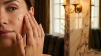 Young woman applying skincare cream to face in elegant bathroom with golden lighting for daily beauty routine and self-care wellness lifestyle.