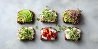 Assortment of healthy open sandwiches with avocado, microgreens, cottage cheese, and cherry tomatoes on whole grain bread against gray background.