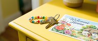 Colorful beaded keychain with house keys resting on a bright yellow table beside a floral welcome home card, symbolizing new beginnings.