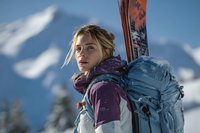 Young blonde woman skier with backpack and skis in snowy mountain landscape ready for winter sports adventure.