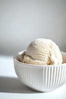 Creamy vanilla ice cream scoop in white ribbed ceramic bowl against light background, minimalist food photography with soft natural lighting and shallow depth of field.