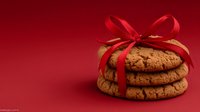 Stack of homemade chocolate chip cookies tied with elegant red ribbon against deep red background, festive holiday treat for gifting or dessert table.