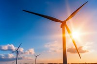 Wind turbines against dramatic sunset sky, renewable energy windmills silhouetted with sun flare and fluffy clouds in background, sustainable power generation.