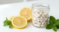 Fresh lemon slices with mint leaves and white supplement capsules in glass jar on clean white surface for natural health and wellness concepts.