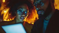 Young African American couple looking at laptop screen with amazed expressions in warm evening lighting, creating intimate atmosphere for remote work or entertainment.