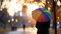 Silhouette of person holding colorful rainbow umbrella at sunset in park with golden bokeh lights and autumn trees creating dreamy atmospheric scene.