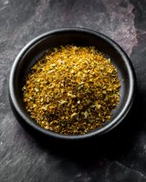Aromatic dried herbs and spices mixture in black ceramic bowl on dark stone background, macro food photography for cooking and seasoning concepts.